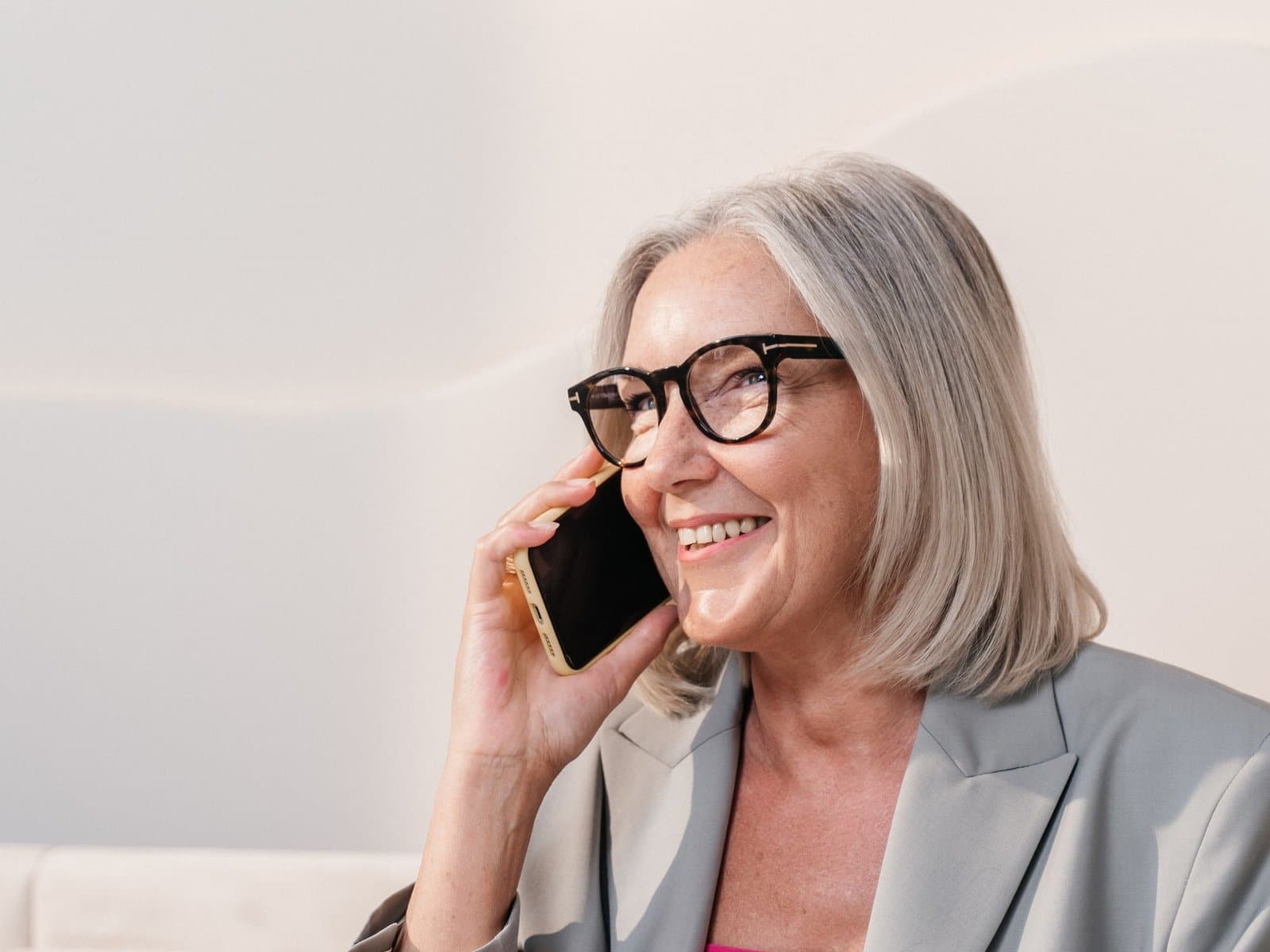 A smiling older woman with glasses talking on her phone at home