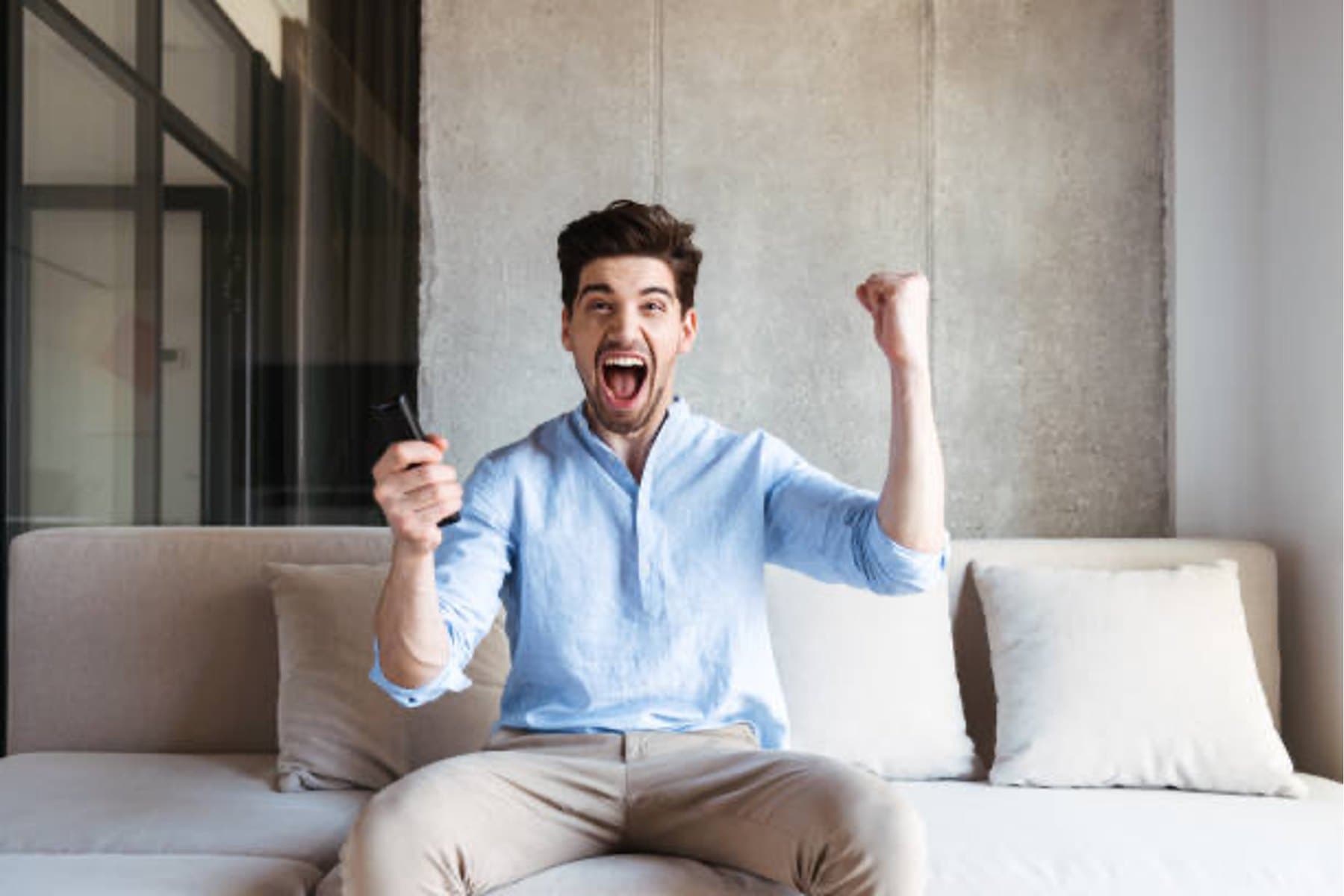 A man on a couch celebrating with a raised fist after hearing good news